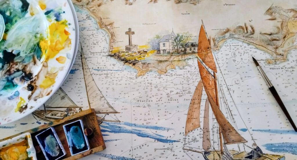 Vue de dessus d'un atelier d'artiste montrant une carte marine illustrée à l'aquarelle de voiliers et de côtes, entourée d'une palette de peinture, de godets et d'un pinceau