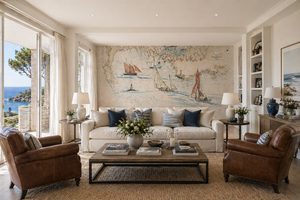 salon-decoration-marine-papier-peint-carte-maritime Salon lumineux au style bord de mer avec un grand canapé blanc, deux fauteuils en cuir marron, et un mur d'accent habillé d'un papier peint panoramique représentant une carte maritime ancienne avec des voiliers