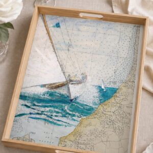 Plateau en bois présentant une aquarelle de voilier naviguant sur une carte marine ancienne, posé sur une table dressée.
